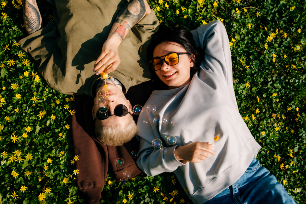 Two people lie in a field of yellow flowers, relaxing in the sun while blowing bubbles.